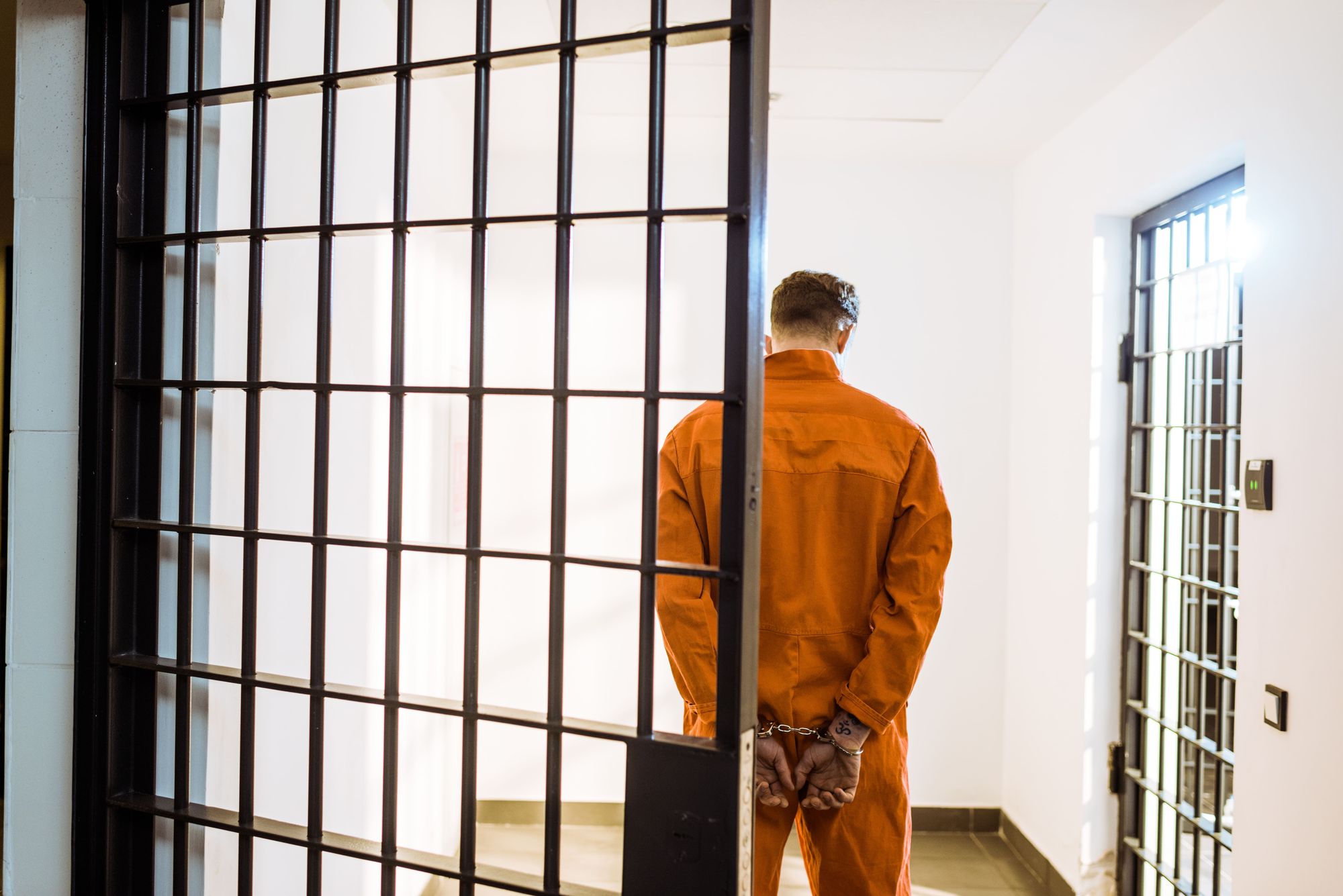 Back view of a prisoner standing in handcuffs in a jail corridor — HHA Law explains whether you can go to jail for not paying debt in the United States